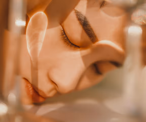 Close-up of a serene person's face with closed eyes, partially obscured by translucent reflections.