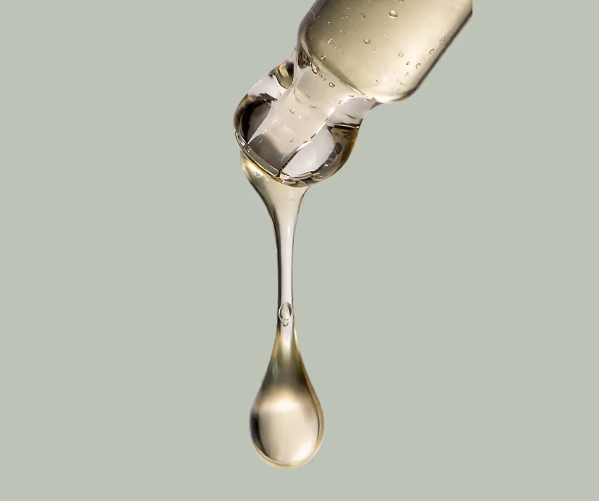 Close-up of a clear dropper releasing a single drop of translucent liquid on a light gray background.